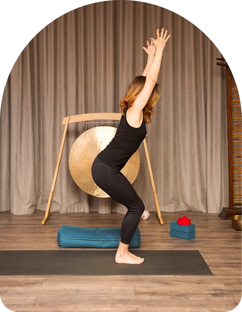 Chair pose with raised arms in front of a gong